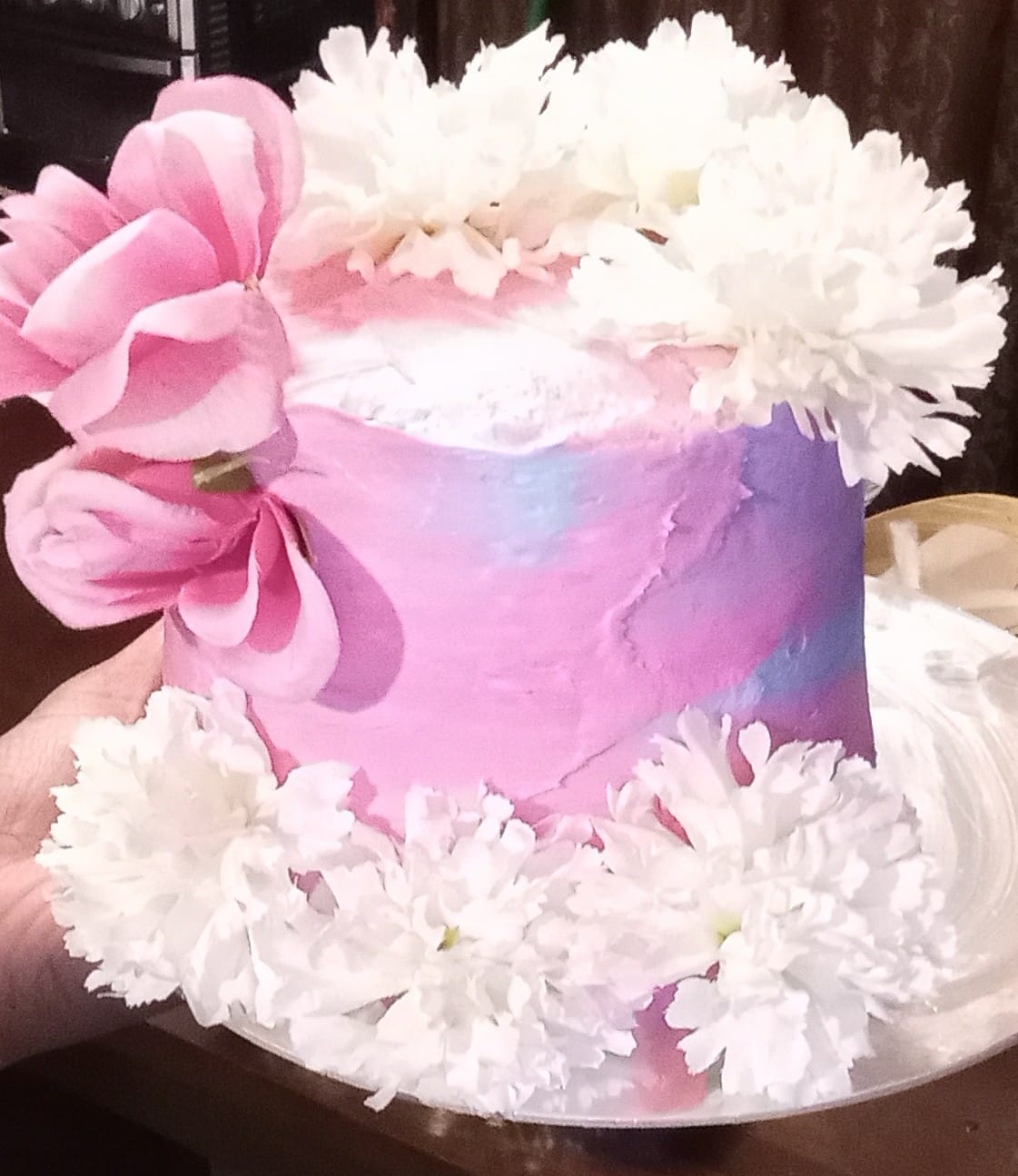 Beautiful purple and blue cake, with white frosting and pink flower decorations.